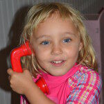 A young girl talking on a red toy phone.