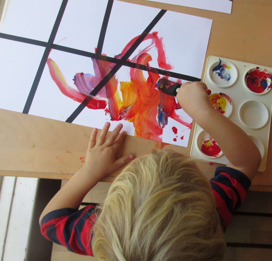 A child painting with red and yellow paint.