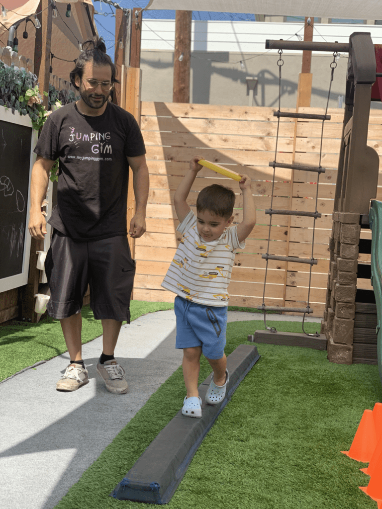 Man watches boy walk on balance beam.