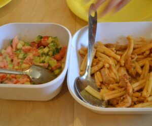 Two containers with cooked pasta and chopped vegetables.