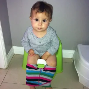 A toddler sitting on a potty with colorful pants pulled down. at Montana preschool