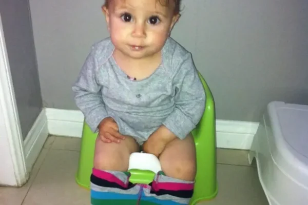 A toddler sitting on a potty with colorful pants pulled down. at Montana preschool