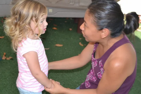 A woman and a young girl holding hands and talking indoors.