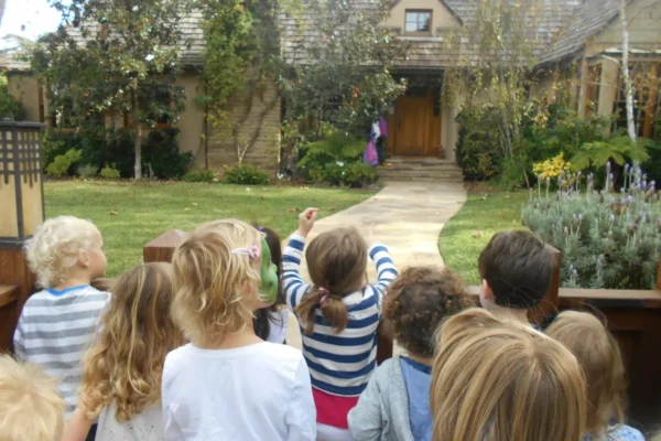 Children watching a person walking towards a house in a garden.